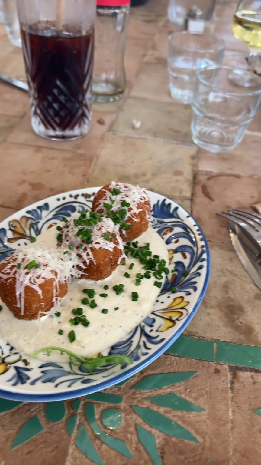 Arancini dorés sur une crème au pecorino et poivre, dans une assiette en céramique bleue et blanche.