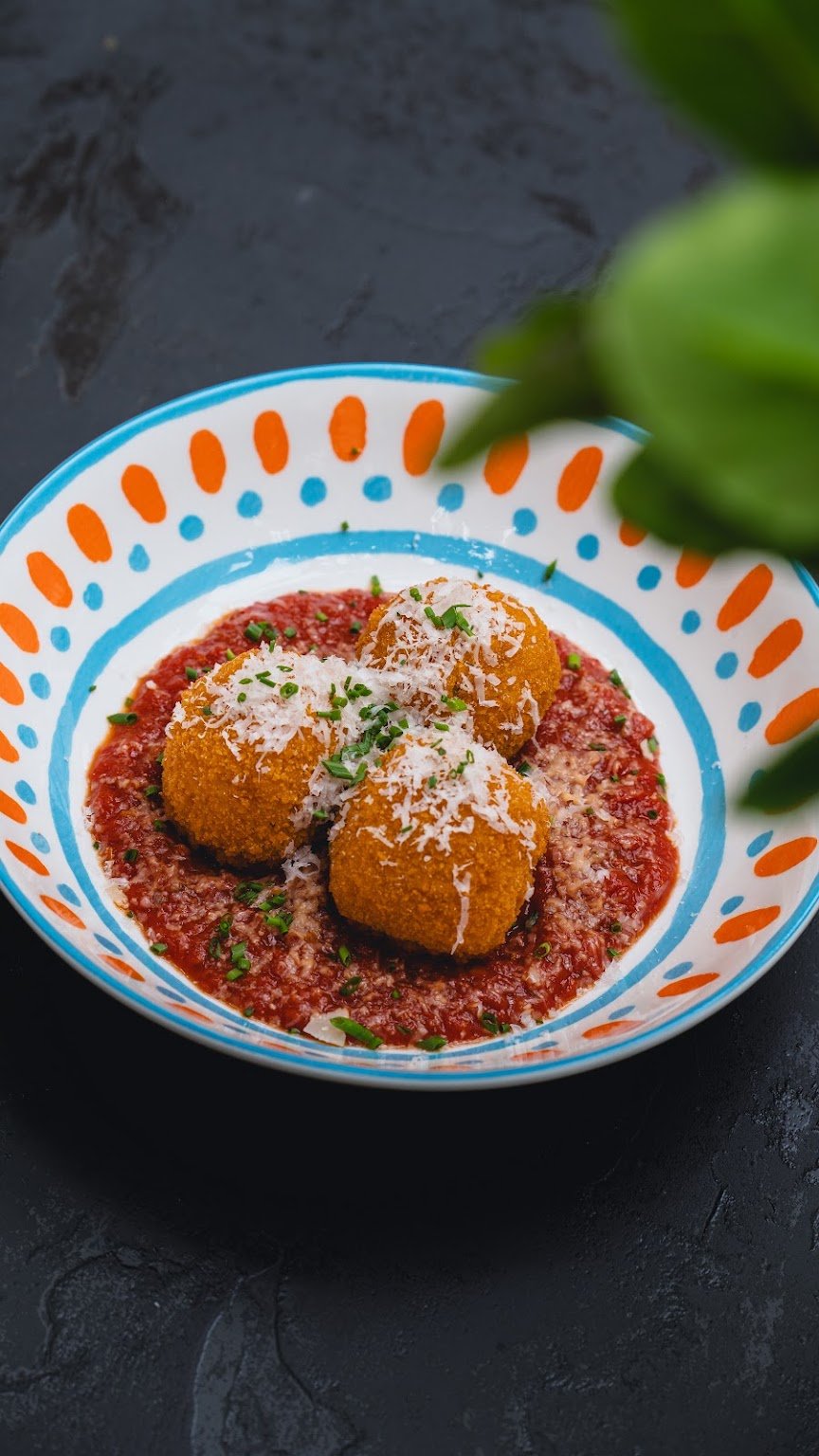 Arancini dans une sauce tomate, parmesan râpé, dans une assiette en céramique bleue et orange.