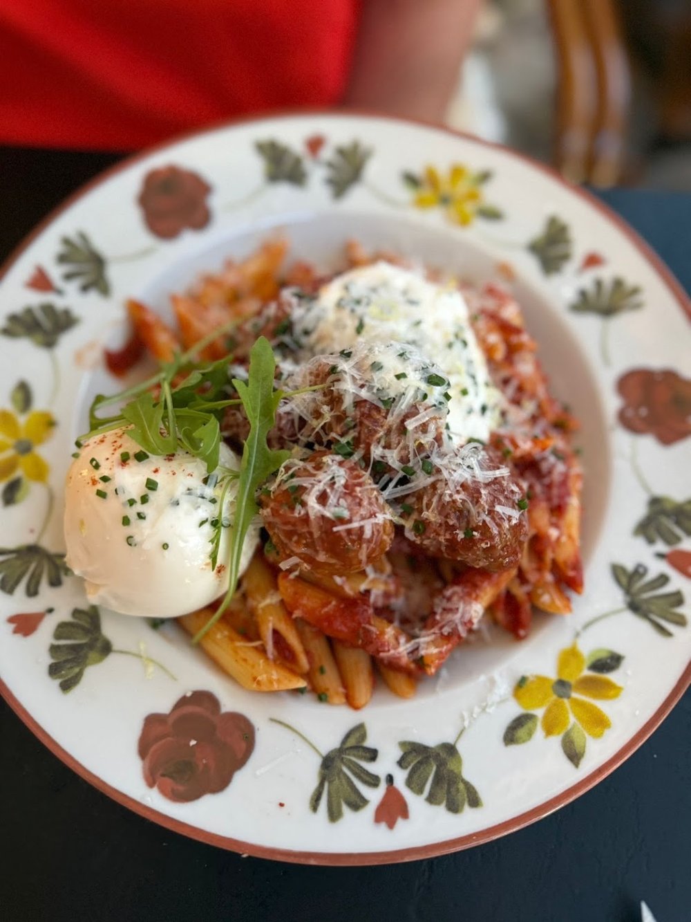 Penne à la sauce tomate garnies de boulettes et d’un cœur de burrata, assiette en céramique à fleurs.
