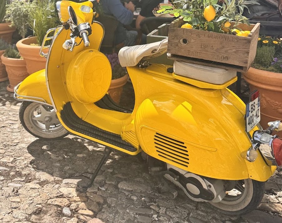 Une Vespa jaune garée sur les pavés de la cour, une caisse en bois pleine de citrons sur le porte-bagages.
